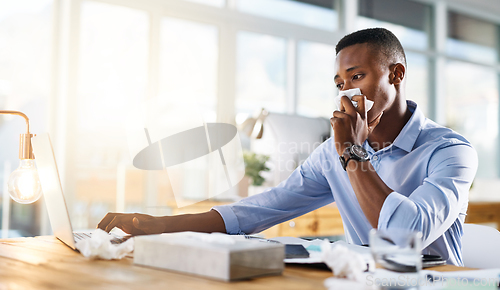Image of This cold isnt going to stop me working. Shot of a young businessman making use of tissues for his cold while trying to work in the office.