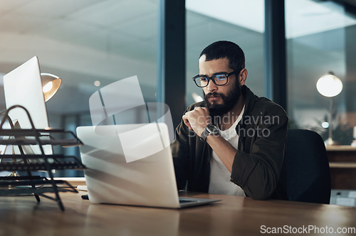 Image of The more you focus the quicker youll find the solution. Shot of a young businessman using a laptop during a late night in a modern office.