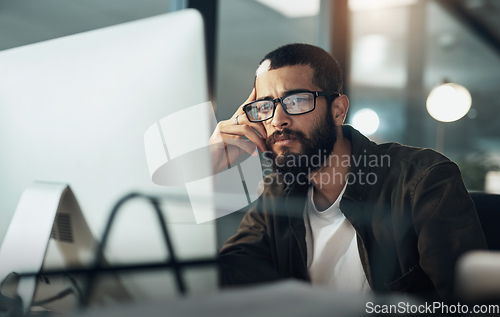 Image of The later it gets the deeper he goes. Shot of a young businessman using a computer during a late night in a modern office.