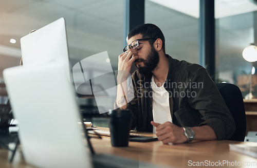 Image of How many more nights of this can I take. Shot of a young businessman feeling stressed while working late at night in a modern office.
