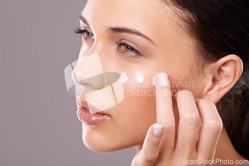 Image of Giving her skin the hydration it needs. Studio shot of a beautiful young woman applying a skincare product to her face.