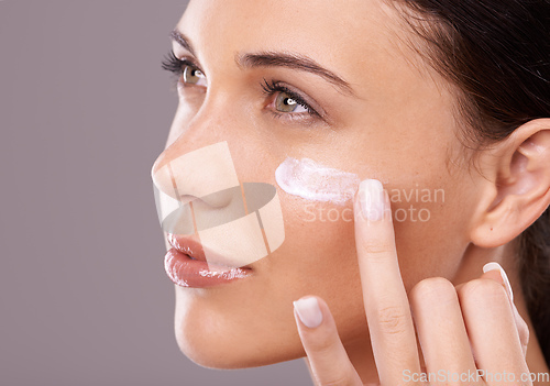 Image of Showing her skin some love. Studio shot of a beautiful young woman applying a skincare product to her face.