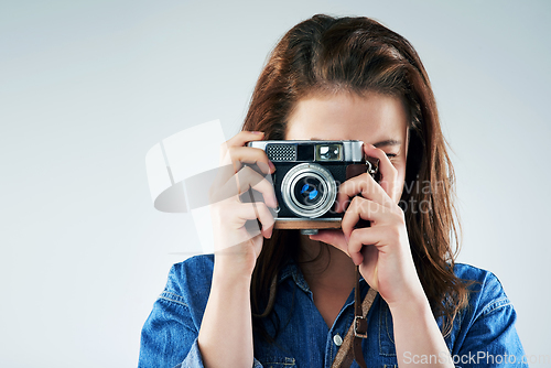 Image of Retro is the way to go. Studio portrait of a young woman using a vintage camera against a grey background.
