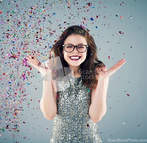 Image of Toss some confetti in the air and celebrate. Studio shot of a young woman with confetti falling around her against a grey background.