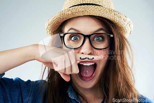 Image of Dont take life too seriously. Studio portrait of a young woman holding her finger under her nose with a moustache drawn on it.