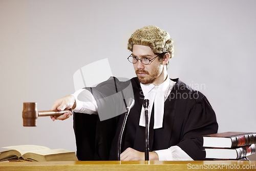 Image of Silence. Serious young judge sitting in the courtroom with a stern facial expression while holding out a gavel.