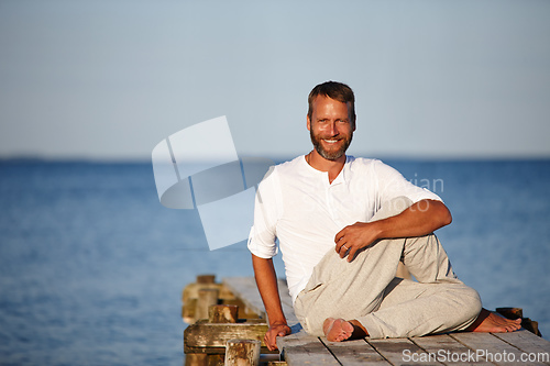 Image of Stretching his muscles to stay flexible. Portrait of a handsome mature man doing yoga on a pier out on the ocean.