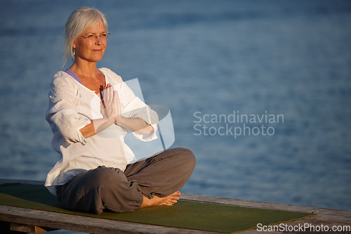 Image of Tranquility by the ocean. Shot of an attractive mature woman doing yoga on a pier out on the ocean.