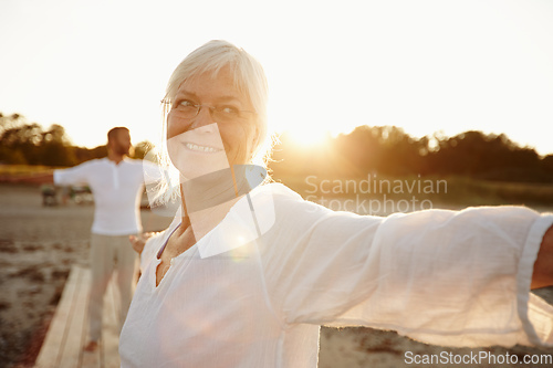 Image of Every day is a yoga day. Shot of a mature woman doing yoga on the beach with her husband in the background.