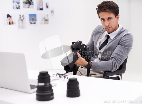 Image of Young and creative photographer. Portrait of a photographer sitting at a desk in his office holding a camera.