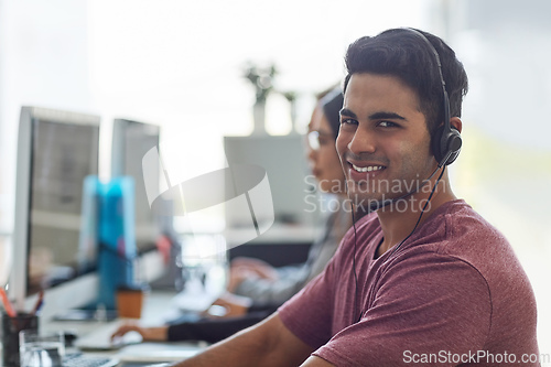 Image of Hes next in line for a promotion. Shot of a young man wearing a headset with his colleagues blurred in the background.