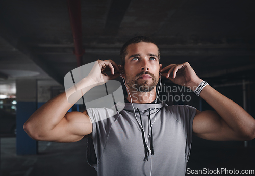 Image of Music is my motivation. Shot of a handsome young sportsman listening to music on his earphones while exercising inside a parking lot.