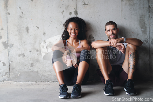 Image of Were down but not out. Portrait of a sporty young couple sitting down against a wall while exercising inside a parking lot.