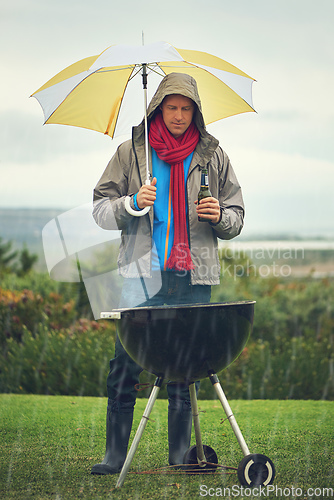 Image of Real men bbq anytime. Shot of a man barbecuing in the rain.