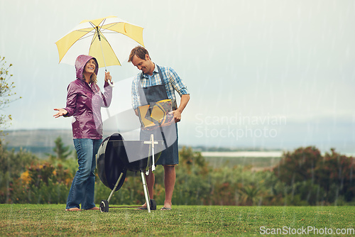 Image of We barbecue anytime, anywhere. Shot of a couple happily barbecuing in the rain.