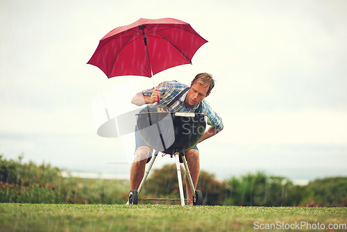 Image of The rain wont stop my barbecue. Shot of a man trying to barbeque in the rain.