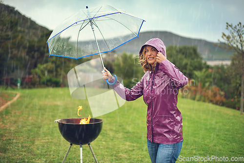 Image of Only the brave barbeque in the rain. Shot of a woman holiding an umbrella while trying to barbeque in the rain.