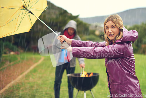 Image of I think its clearing up. Shot of a couple trying to barbecue in the rain.