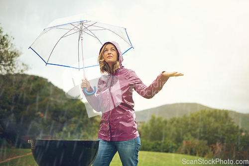 Image of Everything is looking better now. Shot of a woman having a barbecue outside in the rain while holding an umbrella and looking up into the sky.