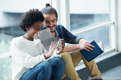 Image of What did she say. A college couple sitting closely together looking at a message on one of their phones.