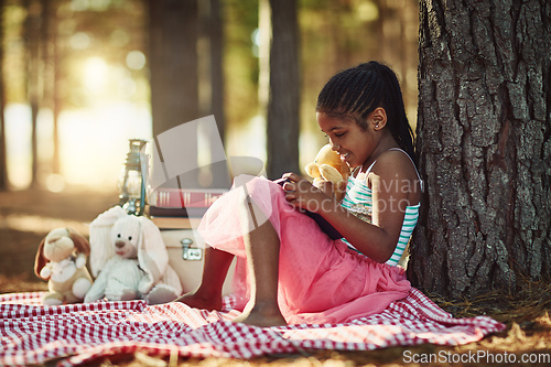 Image of Story time with her favourite little teddy. Shot of a little girl reading a book with her toys in the woods.