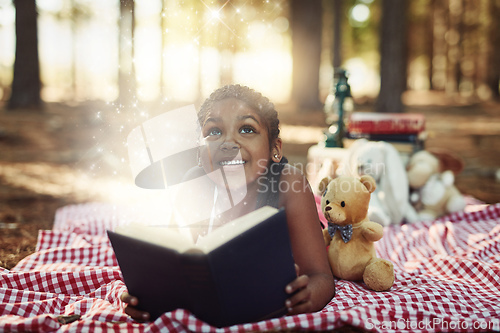 Image of Let reading take you to a magical and wonderful world. Shot of a little girl reading a book with glowing pages in the woods.