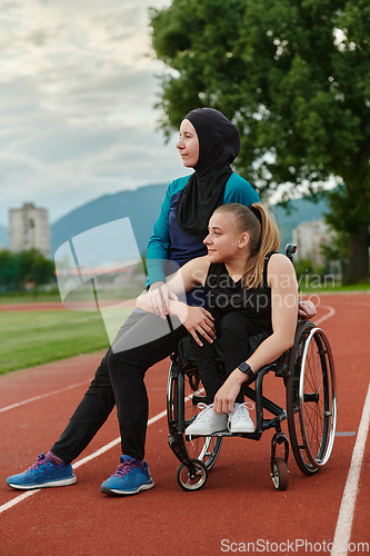 Image of A Muslim woman wearing a burqa resting with a woman with disability after a hard training session on the marathon course