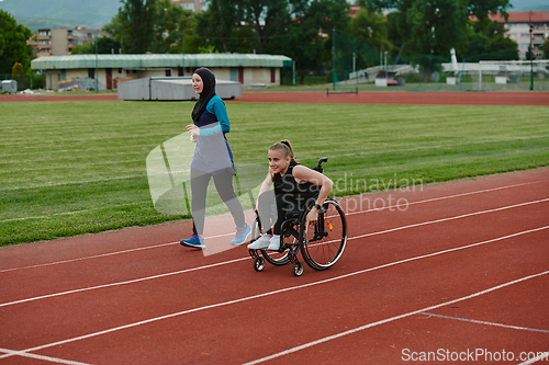 Image of A Muslim woman in a burqa running together with a woman in a wheelchair on the marathon course, preparing for future competitions.