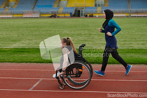 Image of A Muslim woman in a burqa running together with a woman in a wheelchair on the marathon course, preparing for future competitions.