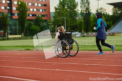 Image of A Muslim woman in a burqa running together with a woman in a wheelchair on the marathon course, preparing for future competitions.