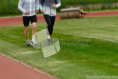 Image of An inspiring and active elderly couple showcase their dedication to fitness as they running together on a lush green field, captured in a close-up shot of their legs in motion.