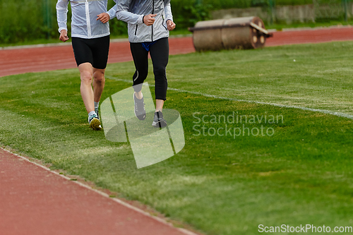 Image of An inspiring and active elderly couple showcase their dedication to fitness as they running together on a lush green field, captured in a close-up shot of their legs in motion.