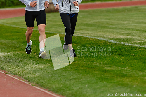 Image of An inspiring and active elderly couple showcase their dedication to fitness as they running together on a lush green field, captured in a close-up shot of their legs in motion.