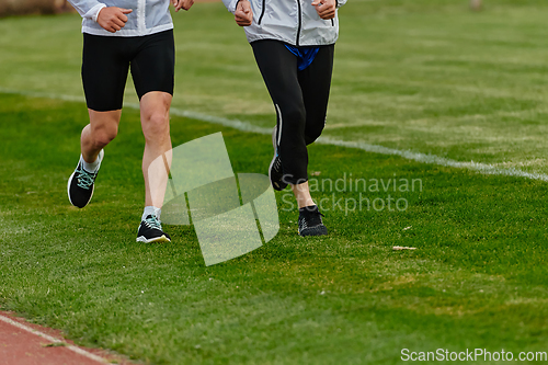 Image of An inspiring and active elderly couple showcase their dedication to fitness as they running together on a lush green field, captured in a close-up shot of their legs in motion.