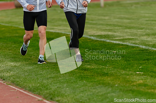 Image of An inspiring and active elderly couple showcase their dedication to fitness as they running together on a lush green field, captured in a close-up shot of their legs in motion.