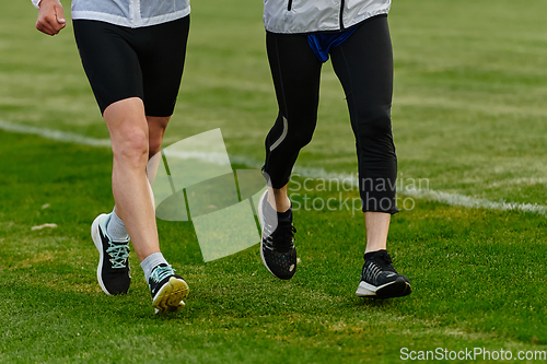 Image of An inspiring and active elderly couple showcase their dedication to fitness as they running together on a lush green field, captured in a close-up shot of their legs in motion.