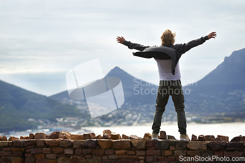 Image of What a day to be alive. Shot of a young man standing on a wall looking at the natural scenery.