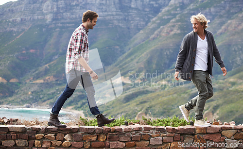 Image of Bonding with my buddy outdoors. Shot of two young men walking on a stone wall with the mountain in the background.