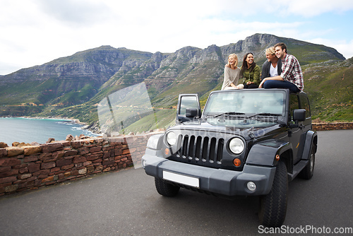 Image of Stopping to experience the breathtaking view. Shot of a group of friends relaxing on the roof of their truck with a mountainous background.