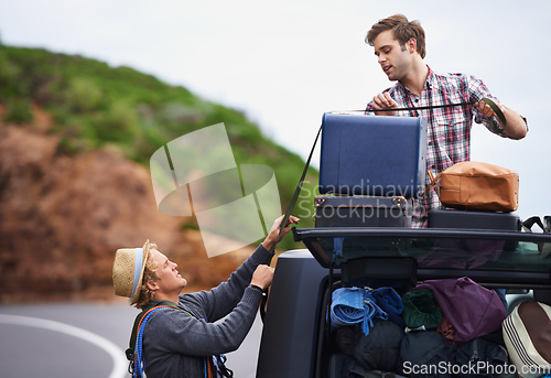 Image of Think we brought too much. Shot of two young men stopped at the side of the road and repacking their truck.