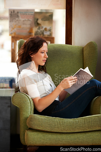 Image of Lost in the story. A young woman sitting in a comfy chair and reading a book.