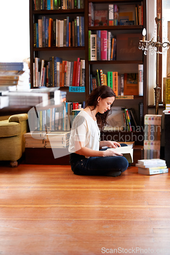 Image of Getting her reading time in. A young woman sitting on the floor with her legs crossed and reading.