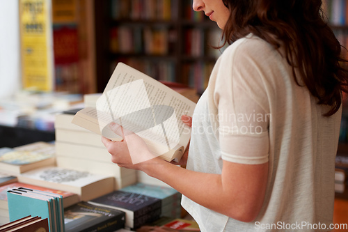 Image of Lost in the pages. A cropped shot of a young woman reading a book while standing in a bookstore.