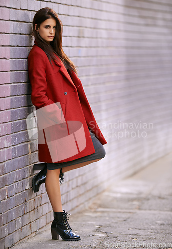 Image of Winter ready in red. Portrait of a gorgeous young woman leaning against a brick wall in the city.