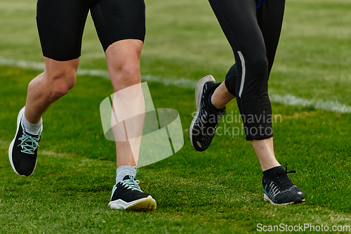 Image of An inspiring and active elderly couple showcase their dedication to fitness as they running together on a lush green field, captured in a close-up shot of their legs in motion.