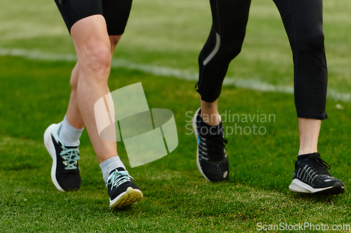 Image of An inspiring and active elderly couple showcase their dedication to fitness as they running together on a lush green field, captured in a close-up shot of their legs in motion.