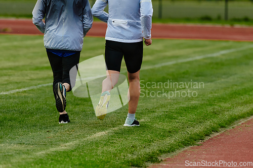 Image of An inspiring and active elderly couple showcase their dedication to fitness as they running together on a lush green field, captured in a close-up shot of their legs in motion.