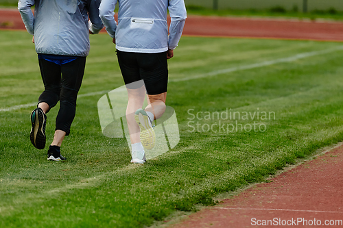 Image of An inspiring and active elderly couple showcase their dedication to fitness as they running together on a lush green field, captured in a close-up shot of their legs in motion.