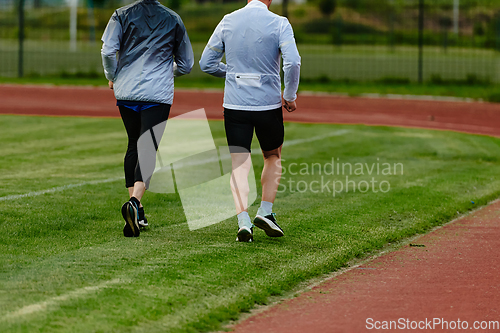 Image of An inspiring and active elderly couple showcase their dedication to fitness as they running together on a lush green field, captured in a close-up shot of their legs in motion.