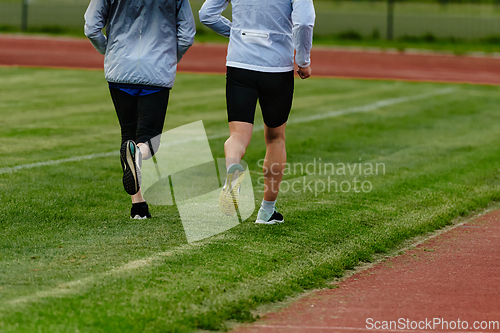 Image of An inspiring and active elderly couple showcase their dedication to fitness as they running together on a lush green field, captured in a close-up shot of their legs in motion.